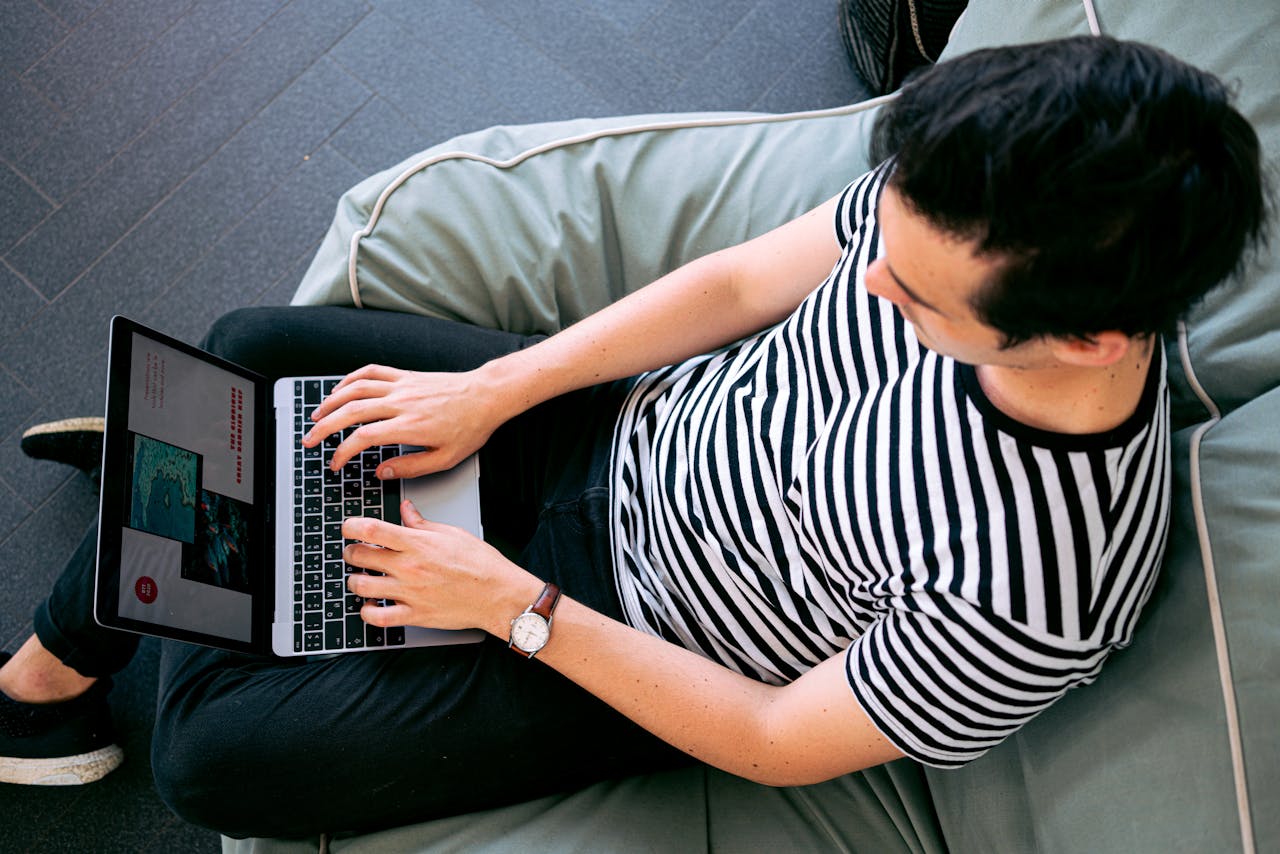 A man in a striped shirt using a laptop on a bean bag, embodying relaxed productivity.